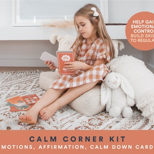K&ouml;nnte beinhalten: Ein Kind sitzt auf einem wei&szlig;en Kissen mit einem wei&szlig;en Stoffhasen und einem Satz bunter Karten, auf denen "Calm Corner Kit: Emotions, Affirmation, Calm Down Cards" steht. Die Karten sollen Kindern helfen, emotionale Kontrolle zu gewinnen und F&auml;higkeiten zur Regulierung ihrer Emotionen aufzubauen.