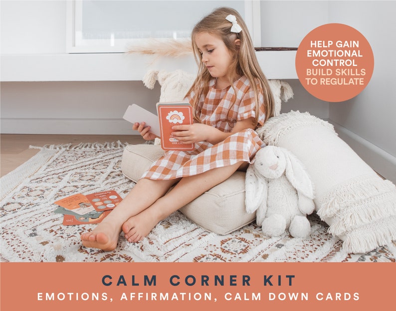 K&ouml;nnte beinhalten: Ein Kind sitzt auf einem wei&szlig;en Kissen mit einem wei&szlig;en Stoffhasen und einem Satz bunter Karten, auf denen "Calm Corner Kit: Emotions, Affirmation, Calm Down Cards" steht. Die Karten sollen Kindern helfen, emotionale Kontrolle zu gewinnen und F&auml;higkeiten zur Regulierung ihrer Emotionen aufzubauen.