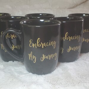 May include: Set of six black ceramic mugs with gold lettering that reads "Embracing My Journey".