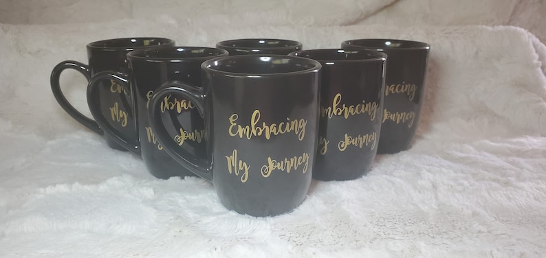 May include: Set of six black ceramic mugs with gold lettering that reads "Embracing My Journey".