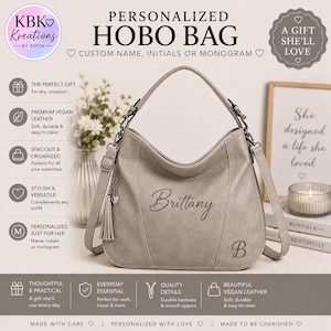 Puede incluir: Un bolso hobo de color gris claro con un asa superior y una correa de hombro ajustable. El bolso está personalizado con el nombre Brittany en letra cursiva y la letra B en fuente serif. Una borla decorativa con un pequeño corazón cuelga del lateral.
