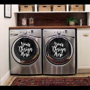 Op de afbeelding: Twee zilveren wasmachines met een witte achtergrond. De wasmachines hebben een ronde, zwarte opening met de tekst "Your Design Here" in wit.