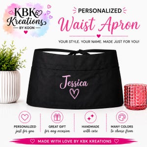 May include: A black waist apron featuring the name Jessica in pink script font with a pink heart icon below it. The apron has a tie-back closure and front pockets. Text on the image includes KBK Kreations, Personalized Waist Apron, and Made with love by KBK Kreations.
