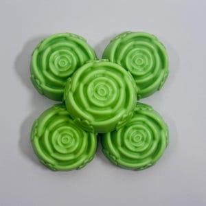 May include: Five round, green soaps arranged in a cluster. Each soap has a spiral design in the center, resembling a rose. The soaps are a vibrant, solid green color and are set against a white background.
