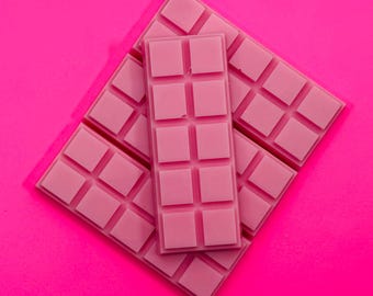 Puede incluir: Una colección de fundentes de cera rosas dispuestos en una pila. Los fundentes son rectangulares con una cuadrícula de pequeños segmentos cuadrados. La pieza superior está orientada verticalmente sobre las piezas base.