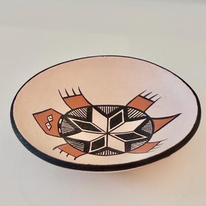 May include: A white ceramic mug with a black handle and the text "But First, Coffee" in a bold, black font. The mug is sitting on a wooden surface. The mug is approximately 4 inches tall.