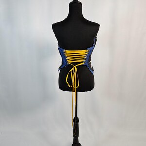 May include: A blue and black corset with yellow lacing is displayed on a black mannequin. The corset has a strapless design and is made of a textured fabric. The mannequin is on a black stand against a white background.
