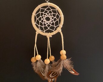 May include: A small beige dreamcatcher with white netting, brown feathers, and wooden beads hanging from a silver key ring.