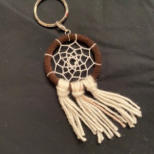 May include: A small brown dreamcatcher keychain with white string and tassels. The dreamcatcher has a silver ring attached to it.