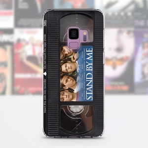 May include: A phone case featuring a VHS tape design with the movie title "Stand By Me." The case has a black and gray VHS tape design with the movie's poster art. The text "Insert this side into recorder" is visible.