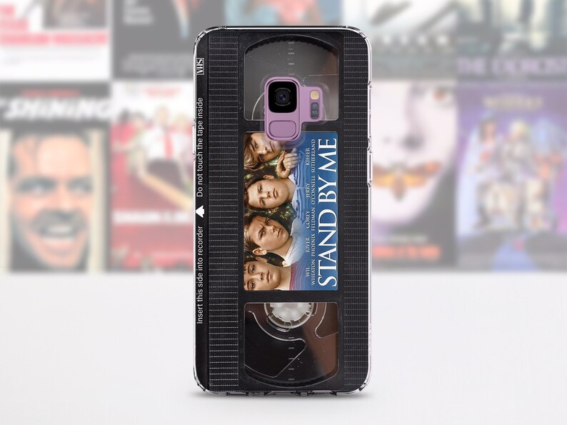 May include: A phone case featuring a VHS tape design with the movie title "Stand By Me." The case has a black and gray VHS tape design with the movie's poster art. The text "Insert this side into recorder" is visible.