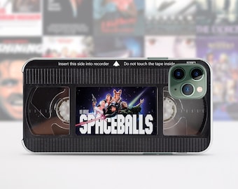 May include: A black and clear phone case with a vintage VHS tape design. The case features the movie title "SPACEBALLS" and a scene from the movie. The case has a black and white striped pattern and the text "Insert this side into recorder" and "Do not touch the tape inside".
