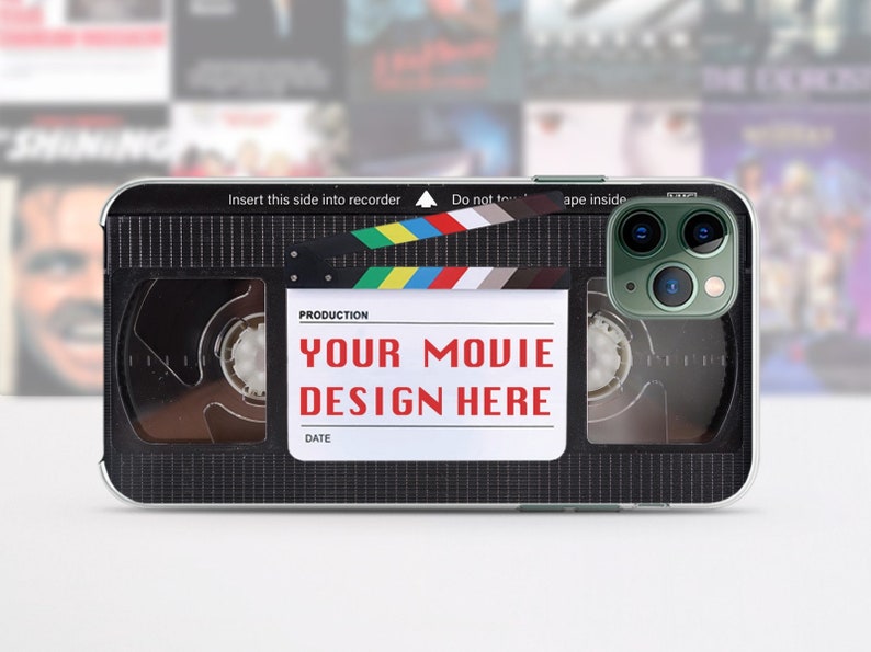 May include: A black and silver phone case with a vintage VHS tape design. The case has a clear window over the camera lens and features the text "YOUR MOVIE DESIGN HERE".