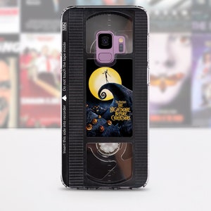 Op de afbeelding: Een zwarte en transparante telefoonhoes met een ontwerp van een VHS-band. De band heeft een label met de tekst "The Nightmare Before Christmas" en een afbeelding van Jack Skellington.