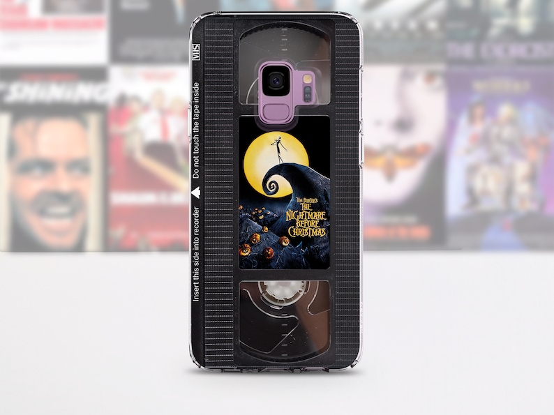 Op de afbeelding: Een zwarte en transparante telefoonhoes met een ontwerp van een VHS-band. De band heeft een label met de tekst "The Nightmare Before Christmas" en een afbeelding van Jack Skellington.