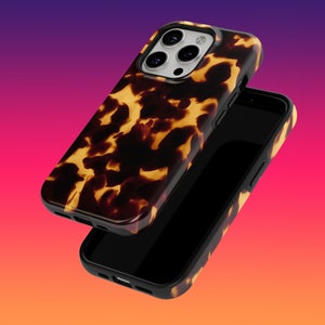 May include: A tortoiseshell-patterned phone case with a black border. The case is shown detached from the phone, revealing the phone's black screen. The case has a glossy finish and a brown and yellow pattern.