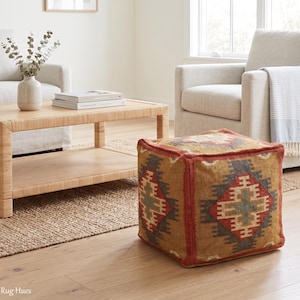 Könnte beinhalten: Ein quadratischer Bodenpouf mit einem gewebten Textilbezug, der ein geometrisches Muster in Rostorange, gedämpftem Grün, Creme und Anthrazit aufweist. Der würfelförmige Hocker hat definierte Kanten und eine strukturierte Oberfläche mit Rautenmuster.