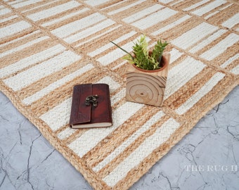 Puede incluir: Una alfombra de fibra natural con un patrón de rayas blancas y beige. La alfombra está hecha de yute y tiene una textura tejida. Una pequeña planta en maceta y un diario encuadernado en cuero se colocan sobre la alfombra.