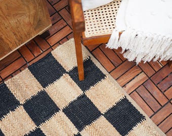 Puede incluir: Una alfombra a cuadros negros y de yute natural con textura tejida. La alfombra está colocada sobre un suelo de madera con un patrón de espiga.