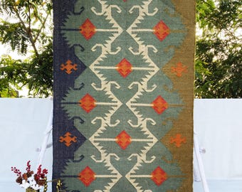 May include: A green, orange, and white patterned rug with a geometric design. The rug has a fringe border and is made of natural fibers.