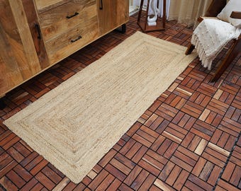 May include: A natural fiber rug in a light beige color with a woven border. The rug is laid on a dark brown wood floor.