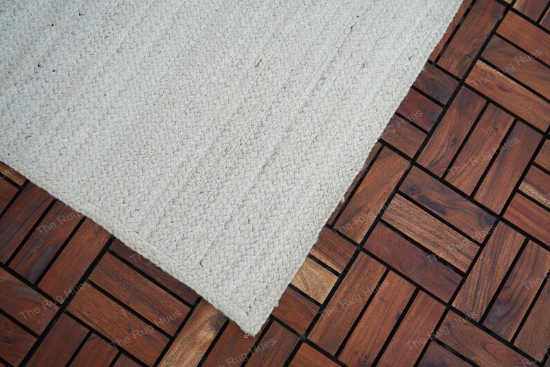 May include: A white woven rug with a textured surface. The rug is placed on a dark brown wood floor.