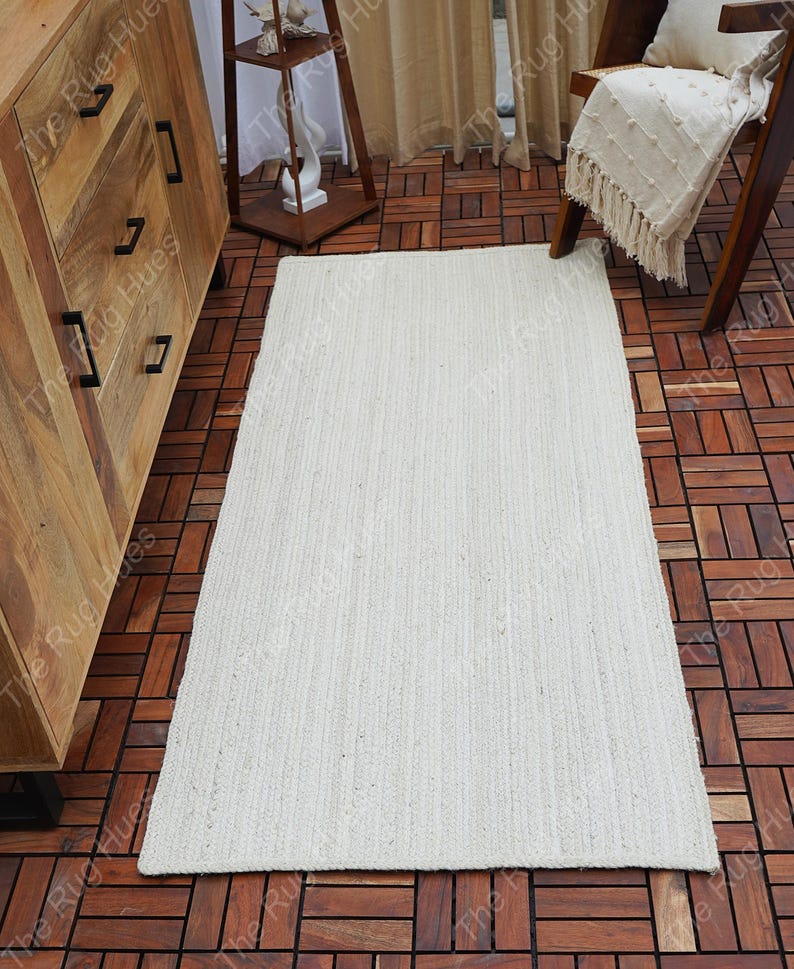 May include: A white, woven, rectangular rug with a subtle texture. The rug is laid out on a wooden floor.