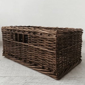 Puede incluir: Una cesta de almacenamiento de mimbre marrón de forma rectangular. La cesta está hecha de mimbre tejido y tiene un acabado natural.