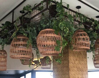 Pode incluir: Um interior de restaurante moderno com um teto coberto de vegetação e luzes pendentes de vime. O restaurante tem uma grande janela com vista para a cidade. Há mesas e cadeiras dispostas para comer.