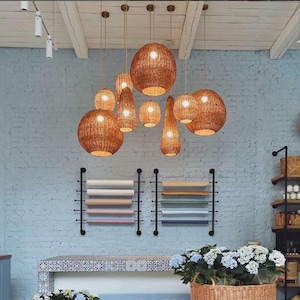 May include: A collection of woven pendant lights hang from the ceiling in a room with white brick walls. The lights are made of natural materials and have a rustic, bohemian style.