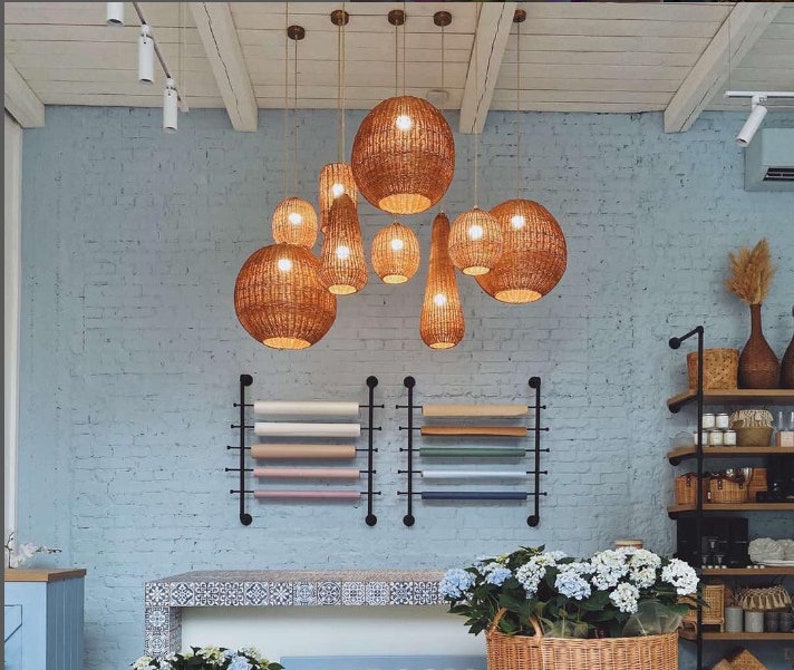 May include: A collection of woven pendant lights hang from the ceiling in a room with white brick walls. The lights are made of natural materials and have a rustic, bohemian style.