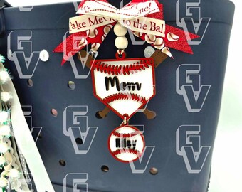 Könnte beinhalten: Eine marineblaue Tragetasche mit einem Baseball-Themen-Anhänger. Der Anhänger zeigt ein Baseballfeld mit dem Wort "Mom" und einen Baseball mit dem Namen "Riley". Ein rot-weißes Band mit dem Text "Take Me to the Ball Game!" ist befestigt.