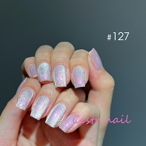 Puede incluir: Primer plano de una mano con varias uñas cuadradas pintadas con un esmalte de brillo rosa claro. Las uñas son cortas y tienen un brillo sutil. El texto #127 y Cestnail son visibles en la imagen.