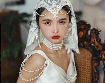 May include: A woman wearing a white lace veil with pearl accents and a white dress with a pearl necklace and pearl shoulder straps.