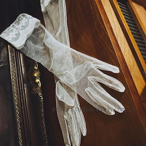 May include: A pair of sheer white opera-length gloves made of a fine mesh fabric. The gloves feature a decorative white lace trim at the wrist openings. The text "ceststudio.etsy.com" is visible in the center of the image on the fabric.