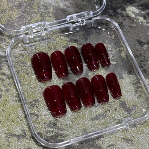 Pode incluir: Uma caixa de pl&aacute;stico transparente com dez unhas posti&ccedil;as de cor bord&ocirc; em forma de caix&atilde;o.