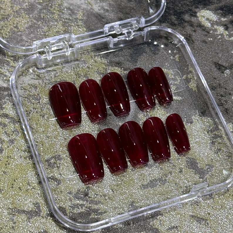 Pode incluir: Uma caixa de pl&aacute;stico transparente com dez unhas posti&ccedil;as de cor bord&ocirc; em forma de caix&atilde;o.