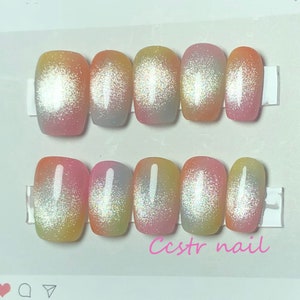 Könnte beinhalten: Set mit zehn kurzen, quadratischen, ombrefarbenen Press-on-Nägeln mit holografischem Glitzer-Finish. Die Nägel sind in den Farben Rosa, Gelb und Blau. Der Text "Ccstr nail" ist in rosa Buchstaben auf weißem Hintergrund geschrieben.