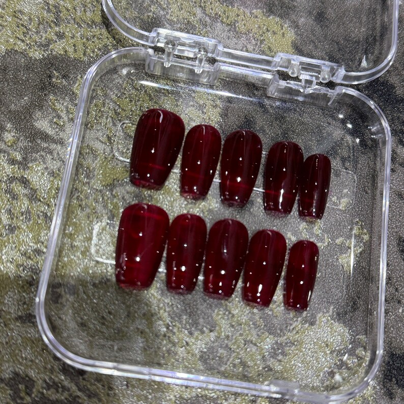 Pode incluir: Um conjunto de dez unhas posti&ccedil;as de caix&atilde;o de cor bord&ocirc; em um recipiente de pl&aacute;stico transparente.