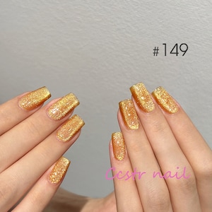Könnte beinhalten: Nahaufnahme von Händen mit goldfarbenem Glitzer-Nagellack. Die Nägel sind kurz und quadratisch geformt. Der Lack ist ein feiner Glitzer mit einer klaren Basis. Das Bild enthält den Text #149 und den Text "cstr nail".