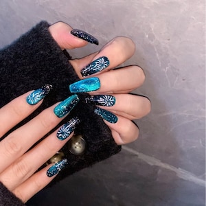 May include: Long, blue and black ombre glitter press-on nails with a white firework design.