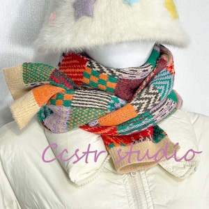 May include: A vibrant, patterned scarf in a patchwork design, featuring red, orange, green, purple, and grey hues. The scarf is worn with a white jacket and a white hat decorated with star-shaped details. The text "CcstrStudio" is visible.