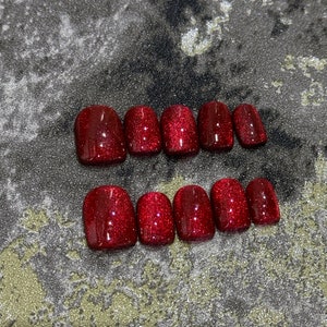May include: Set of ten red glitter press-on nails. The nails are short and oval shaped.