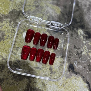 Pode incluir: Uma caixa de pl&aacute;stico transparente com um conjunto de dez unhas posti&ccedil;as vermelhas em forma de caix&atilde;o.