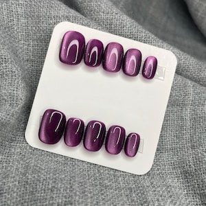 Könnte beinhalten: Ein Set mit zehn lilafarbenen Cat-Eye-Press-on-Nägeln mit einem weißen Schimmereffekt.
