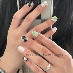 May include: Manicured fingernails featuring a variety of designs including glossy black spheres, textured metallic silver accents, and light green marbled patterns. The nails are displayed against a phone case with the text ccstrstudio.etsy.com :)