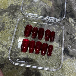 Pode incluir: Uma caixa de pl&aacute;stico transparente com dez unhas posti&ccedil;as vermelhas em forma de caix&atilde;o.