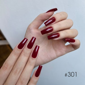 Può includere: Primo piano di una mano con unghie lunghe di colore bordeaux. Le unghie sono tutte della stessa lunghezza e forma, e hanno una finitura lucida. Il testo #301 è visibile nell'angolo in basso a destra dell'immagine.