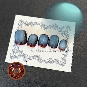 May include: A set of five press-on nails with a gradient design. The nails transition from a deep red at the base to a shimmering blue-gray at the tips. The nails are displayed on a white card with floral border and the text "ccstrstudio.etsy.com".