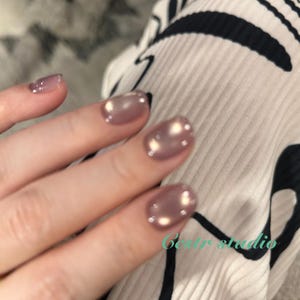 May include: Close-up of a hand with polished nails. The nails are a pearlescent mauve color with small, reflective dots. The ring finger nail is a lighter, translucent mauve. The text "Bestr studio" is visible in the lower right corner.